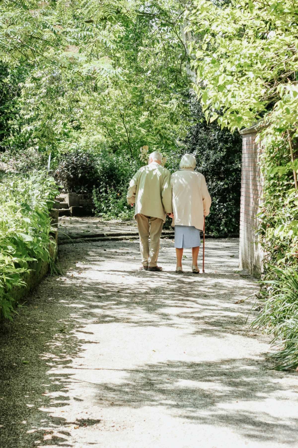 An older couple walking together through a leafy local garden