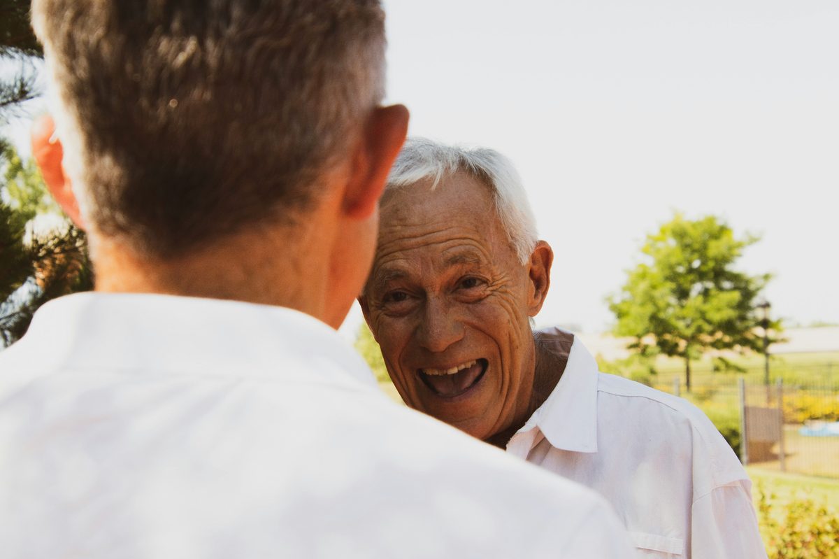 An older man laughing warmly with his companion outdoors